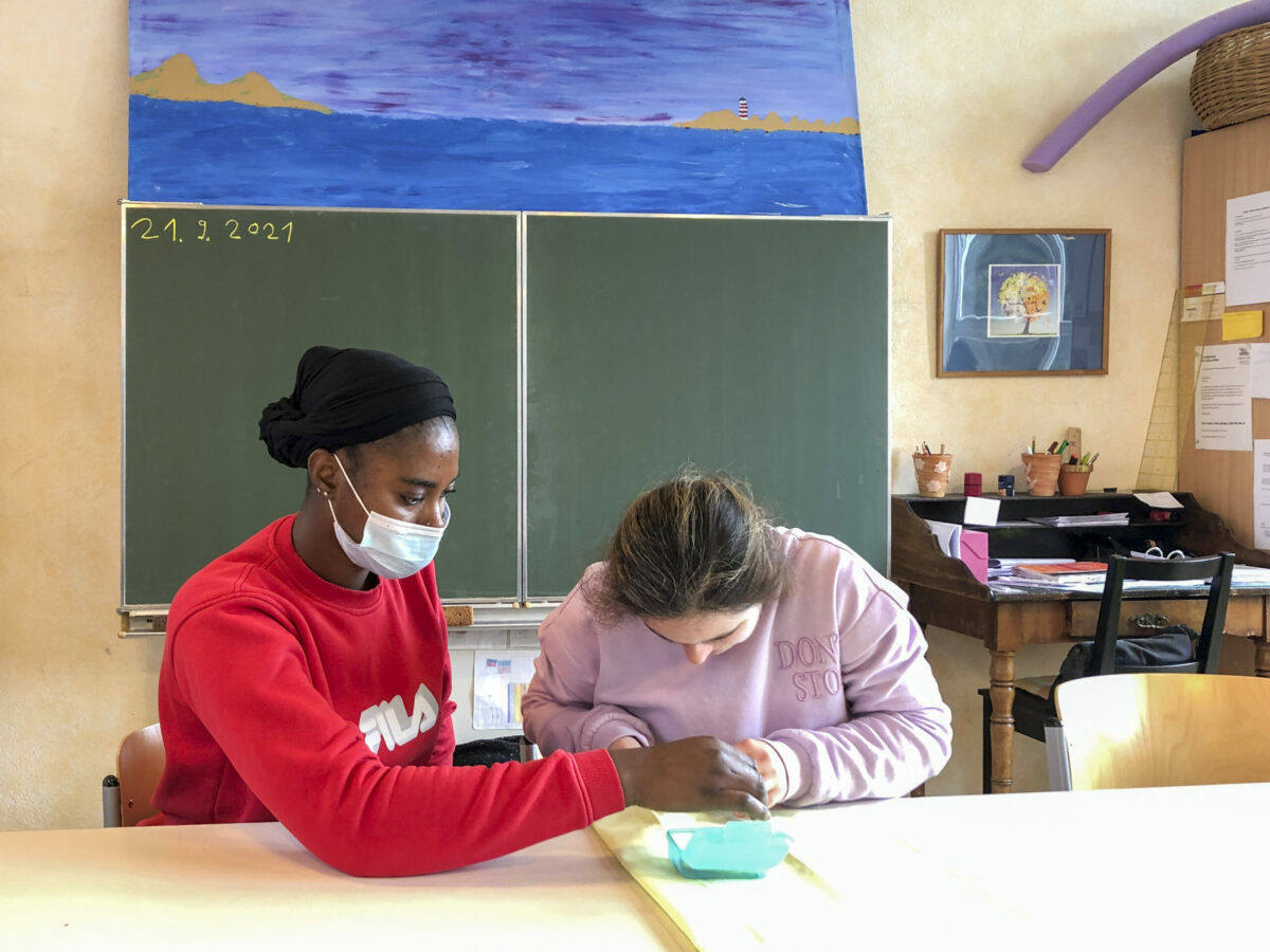 Weltwärts-Bundesfreiwillige Maiama Jabbie aus Gambia leistet den Bundesfreiwilligendienst an der Sonnenhellwegschule (Nähklasse) in Bielefeld: Hier zeigt sie einer Schülerin, wie man einen Kissenstoff absteckt.