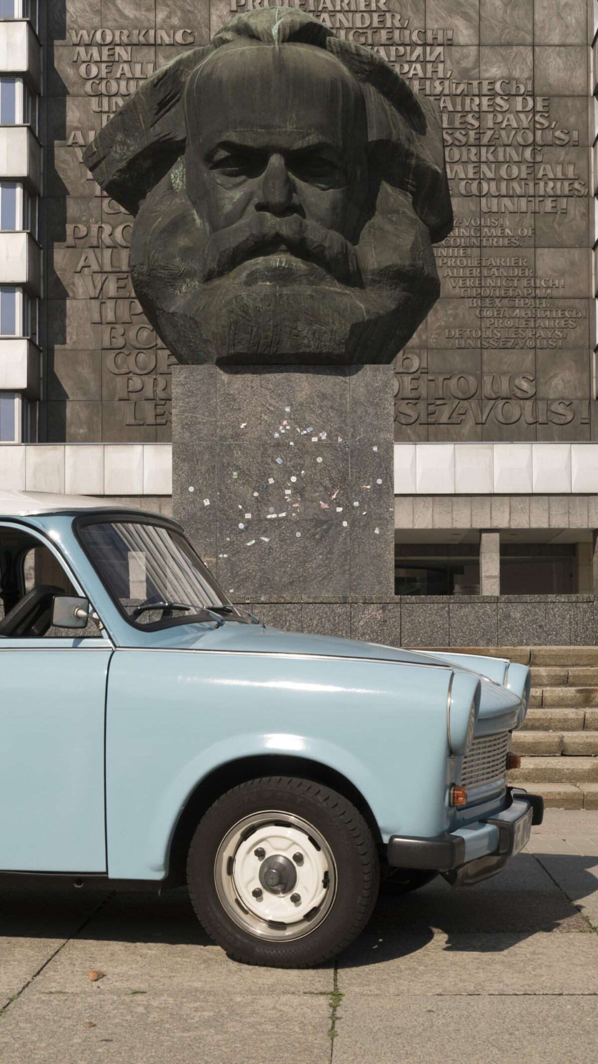 ein hellblauer Trabbi parkt vor dem Karl-Marx-Monument (Nischel) in Chemnitz